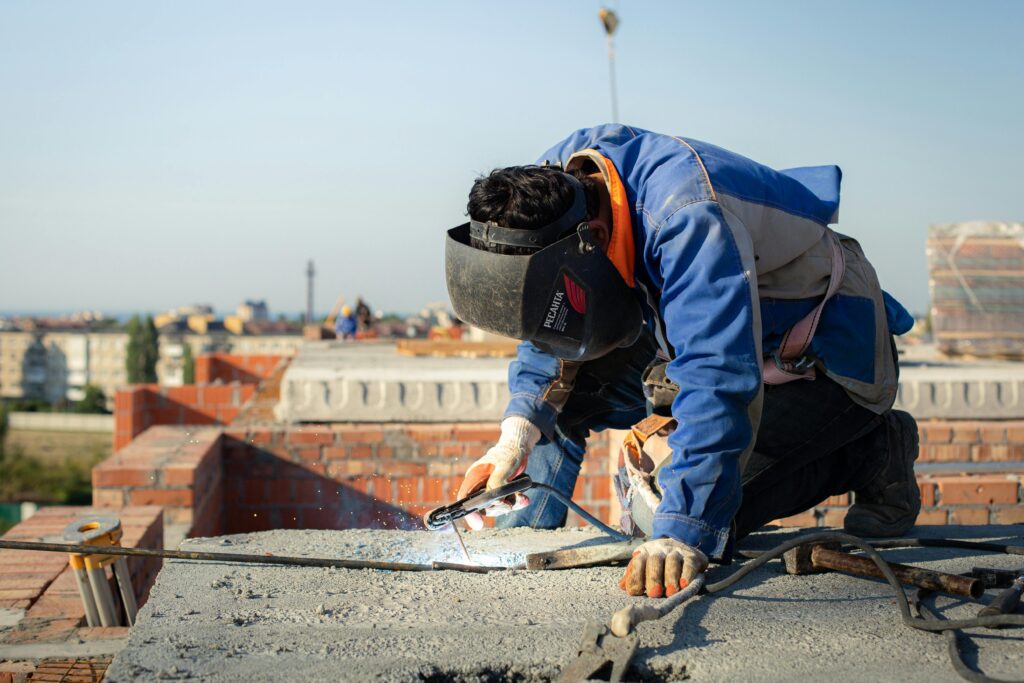 Focused welder in protective gear welding on a city rooftop construction site.